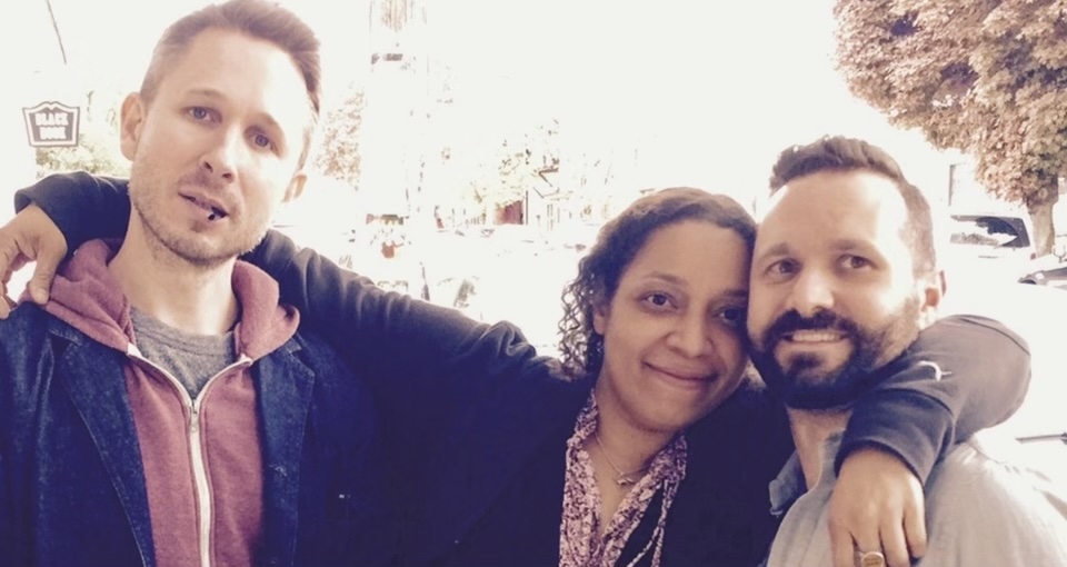 Elliot with two friends, arms around each other on a sunny street