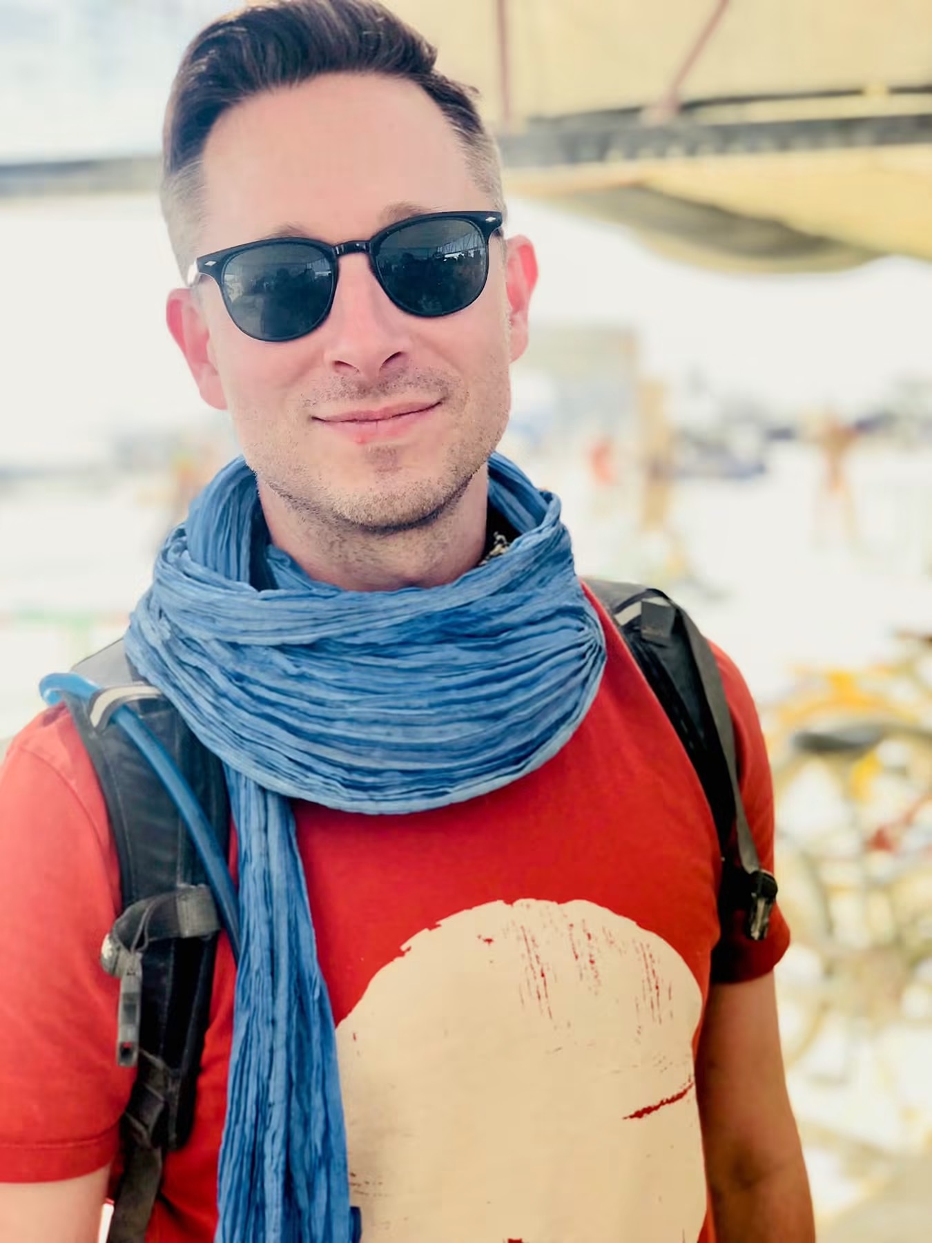 Elliot Graham smiling in the desert, wearing sunglasses and a blue scarf